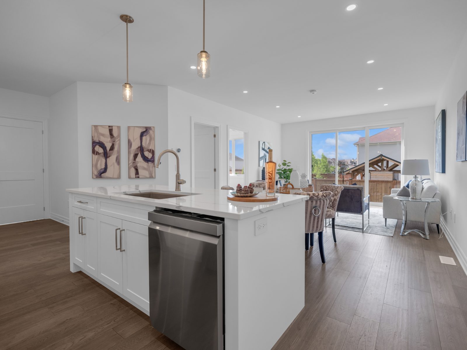 Bright open-concept kitchen with white quartz island, pendant lights and stainless dishwasher flowing into the dining and living area