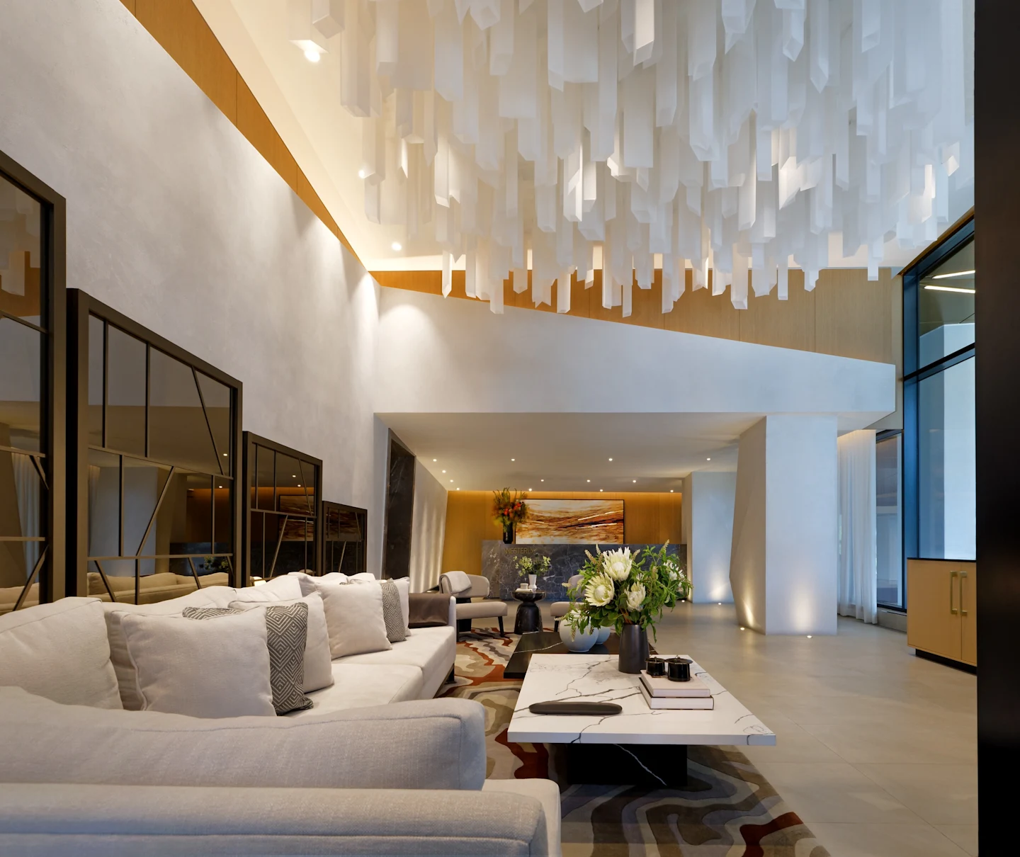 Westerly's double-height lobby lounge with a sculptural white ceiling installation, warm wood accents, marble coffee table and concierge desk