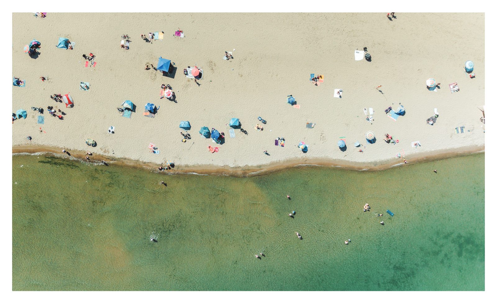 Aerial view of a sandy Lake Ontario beach with umbrellas and swimmers in clear green water